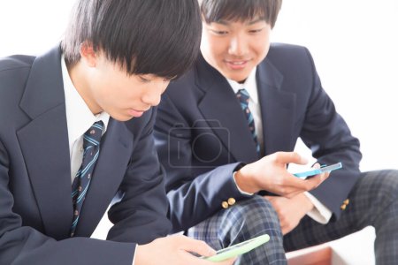 Foto de Dos asiático jóvenes chicos en la escuela uniforme usando móvil teléfonos - Imagen libre de derechos