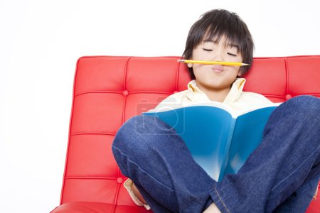 Foto de Niño pequeño leyendo libro en el sofá en casa. - Imagen libre de derechos