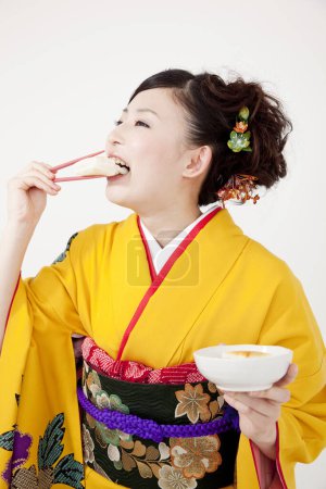 Foto de Mujer joven en kimono comiendo sushi en comida japonesa con palillos - Imagen libre de derechos