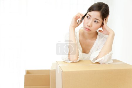 Photo for Woman talking on smartphone with a cardboard box on the floor - Royalty Free Image