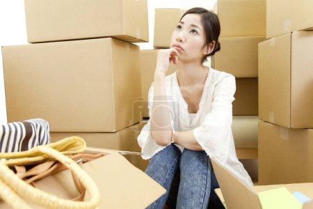 Téléchargez les photos : Jeune femme réfléchie assise avec des boîtes en carton dans une nouvelle maison - en image libre de droit