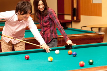 glücklicher japanischer junger Mann und Frau beim Billardspielen
