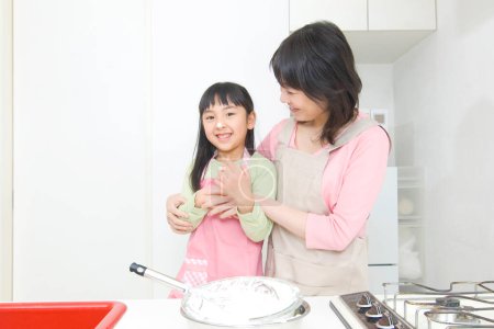 Foto de Sonriente japonesa mujer y su hija cocinar en cocina - Imagen libre de derechos