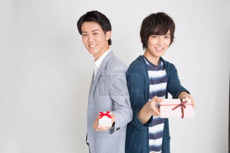 Téléchargez les photos : Portrait de deux beaux jeunes hommes japonais tenant des boîtes-cadeaux sur fond clair - en image libre de droit