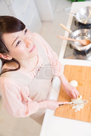 Foto de Hermosa japonesa mujer en delantal llorando mientras corte cebolla en cocina - Imagen libre de derechos