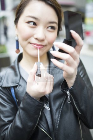 Téléchargez les photos : Jeune femme appliquant gloss lèvre sur la rue - en image libre de droit