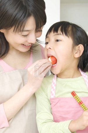 Foto de Sonriente japonesa mujer dando fresa a su hija - Imagen libre de derechos