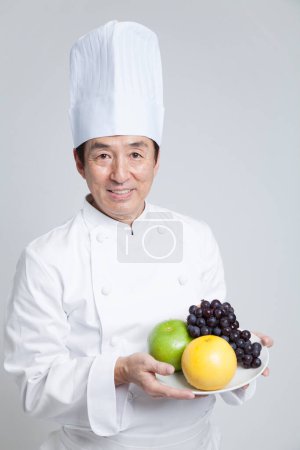 Téléchargez les photos : Asiatique mature chef holding frais fruits - en image libre de droit