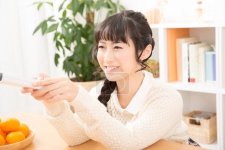 Téléchargez les photos : Asiatique femme tenant télécommande à la maison - en image libre de droit