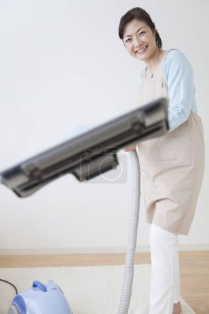 Téléchargez les photos : Asiatique femme nettoyage maison à la maison avec aspirateur - en image libre de droit