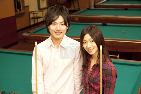 glückliche japanische junge Mann und Frau mit Billard-Queues