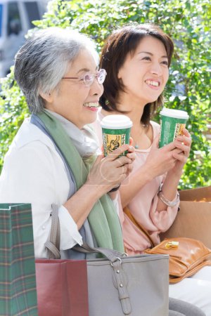 Téléchargez les photos : Femme âgée et jeune femme avec des tasses à café dans la rue - en image libre de droit