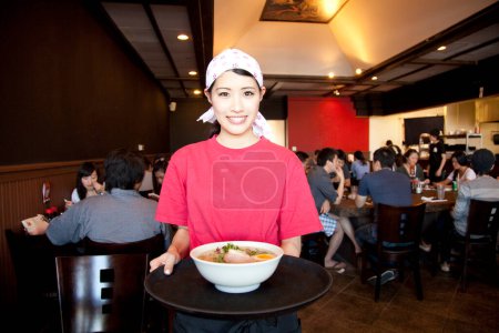 Photo for Asian young waitress with a bowl of noodles in a restaurant - Royalty Free Image