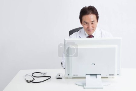 Téléchargez les photos : Asiatique senior médecin travaillant sur ordinateur à l'hôpital. - en image libre de droit