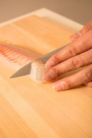Téléchargez les photos : Homme coupe filet de poisson cru frais sur planche en bois - en image libre de droit