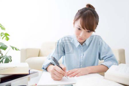 Téléchargez les photos : Jeune femme japonaise étudiant à la maison avec des livres et un stylo - en image libre de droit