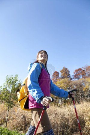 Photo for Young Japanese woman with yellow backpack trekking in autumnal park - Royalty Free Image