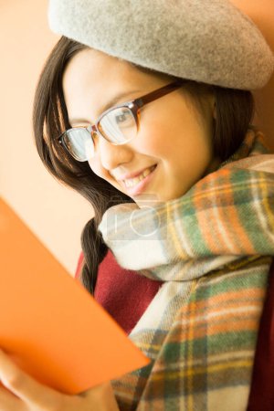 Foto de Feliz asiático mujer leyendo libro en naranja fondo - Imagen libre de derechos
