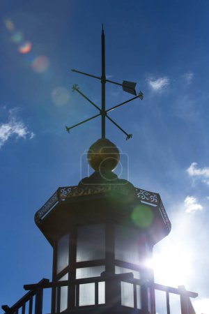 Weather vane placed on a roof, cloudy sky background 
