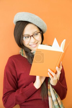 Téléchargez les photos : Heureux asiatique femme lecture livre sur orange fond - en image libre de droit