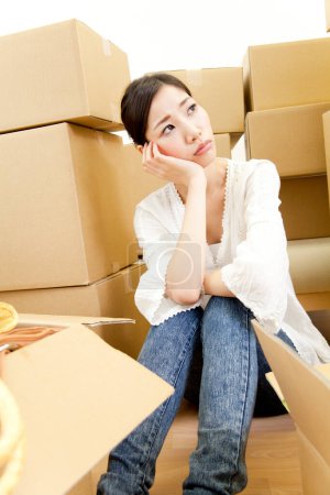 Photo for Thoughtful young woman sitting with cardboard boxes in new home - Royalty Free Image