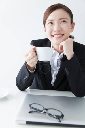 Photo for Portrait of beautiful young Japanese businesswoman drinking coffee at workplace - Royalty Free Image
