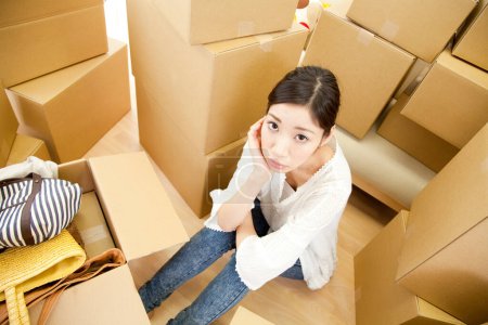 Photo for Thoughtful young woman sitting with cardboard boxes in new home - Royalty Free Image