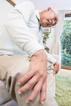Photo for Senior man suffering from pain in knee  on sofa in home - Royalty Free Image