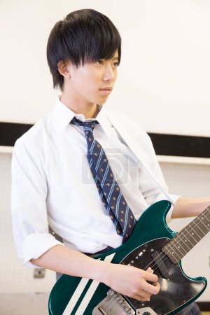 Téléchargez les photos : Japonais écolier jouer de la guitare électrique en classe - en image libre de droit