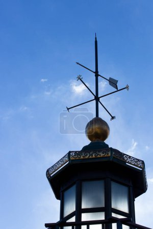 Clack weather vane placed on a roof, cloudy sky background 
