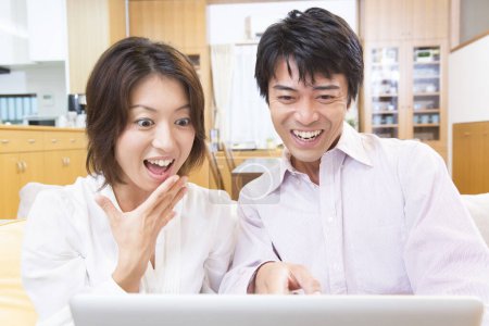 Foto de Joven feliz pareja japonesa utilizando el ordenador portátil en la habitación - Imagen libre de derechos