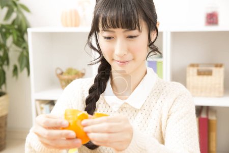 Photo for Young asian woman peeling  tangerine  in the living room - Royalty Free Image