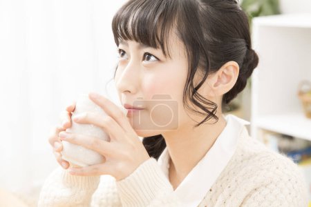 Photo for Asian young woman in white sweater with cup at home - Royalty Free Image