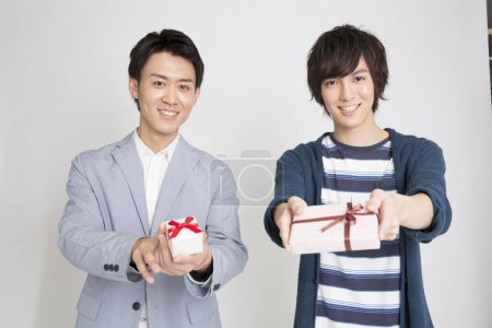 Téléchargez les photos : Portrait de deux beaux jeunes hommes japonais tenant des boîtes-cadeaux sur fond clair - en image libre de droit