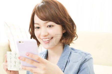 Photo for Beautiful Japanese woman using mobile phone at home - Royalty Free Image
