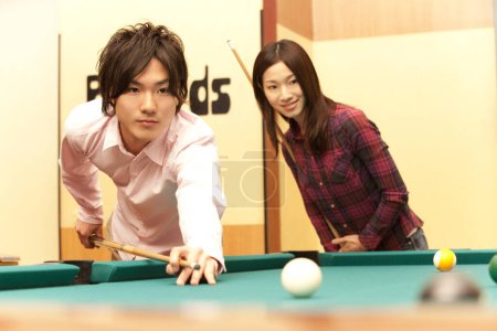 happy Japanese young man and woman playing billiard