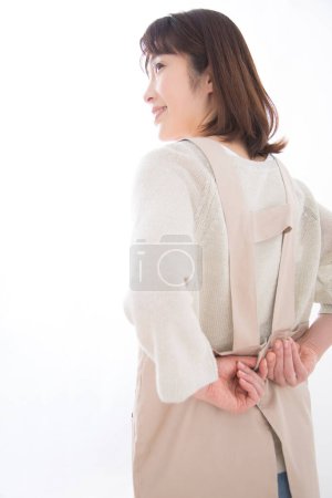 Téléchargez les photos : Jeune femme asiatique en beige tablier posant en studio sur fond blanc - en image libre de droit