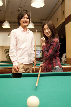 happy Japanese young man and woman playing billiard