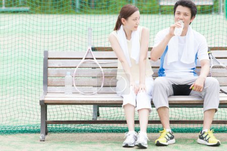 Foto de Joven hombre y mujer en el banco después de jugar al tenis - Imagen libre de derechos