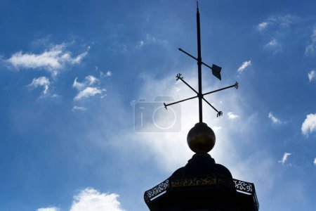 Clack weather vane placed on a roof, cloudy sky background 
