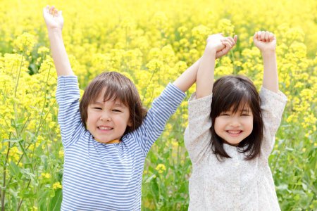 Téléchargez les photos : Enfants japonais mignons avec les mains levées sur le champ de colza - en image libre de droit