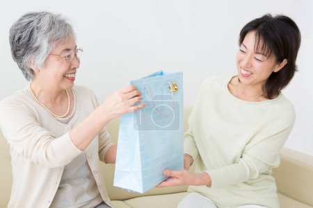 Téléchargez les photos : Asiatique senior femme donnant cadeau à jeune femme - en image libre de droit