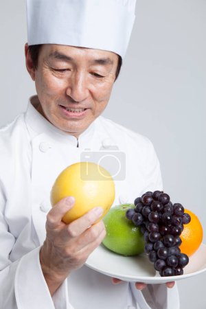 Téléchargez les photos : Asiatique mature chef holding frais fruits - en image libre de droit