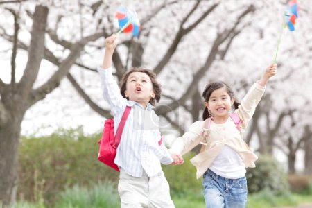 Glückliche japanische Schulkinder mit Windrad im Frühlingspark