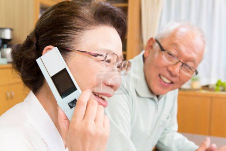 Foto de Asiático senior pareja hablando con inteligente teléfono en casa - Imagen libre de derechos