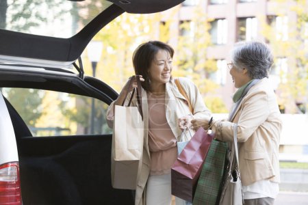 Téléchargez les photos : Femme âgée et sa fille faisant du shopping, debout avec des sacs à provisions en voiture - en image libre de droit