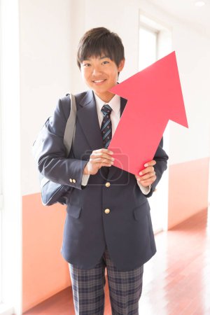 Japanischer Student steht an der Universität und hält roten Pfeil in der Hand 