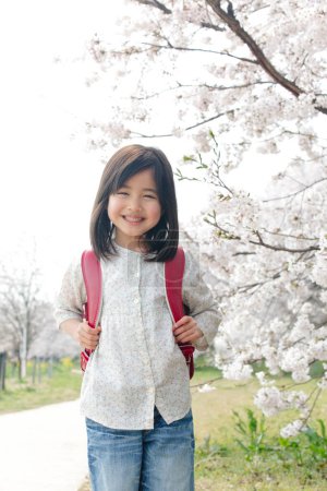 Téléchargez les photos : Mignonne fille japonaise enfant avec sac à dos dans le parc de printemps. concept d'éducation - en image libre de droit