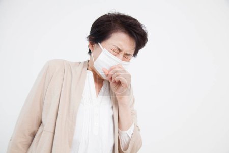 Téléchargez les photos : Portrait de femme japonaise senior avec masque se sentant malade sur fond blanc - en image libre de droit