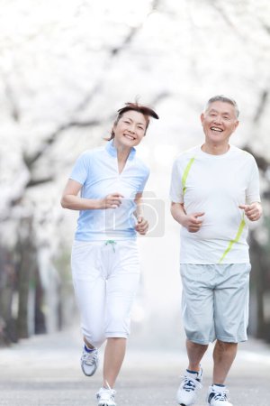 Photo for Asian mature couple running in park with blooming trees - Royalty Free Image